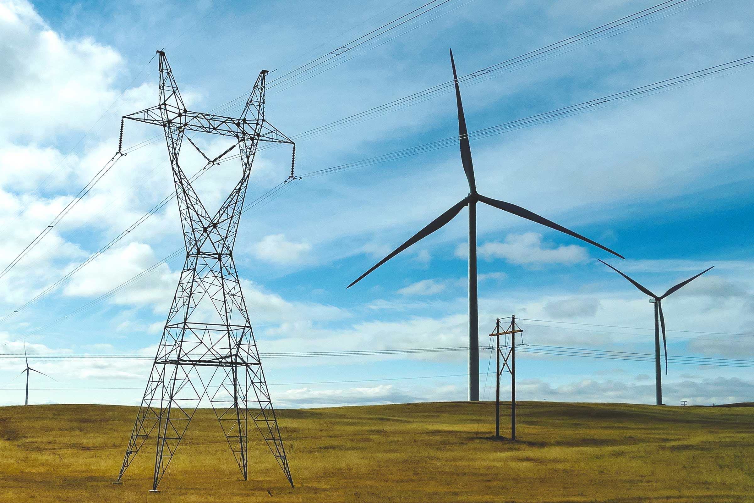 Wind turbines positioned on a plain next to electric grid towers