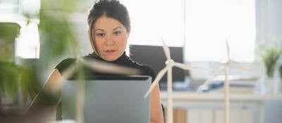 a person with small wind turbine models on a desk, working on a laptop