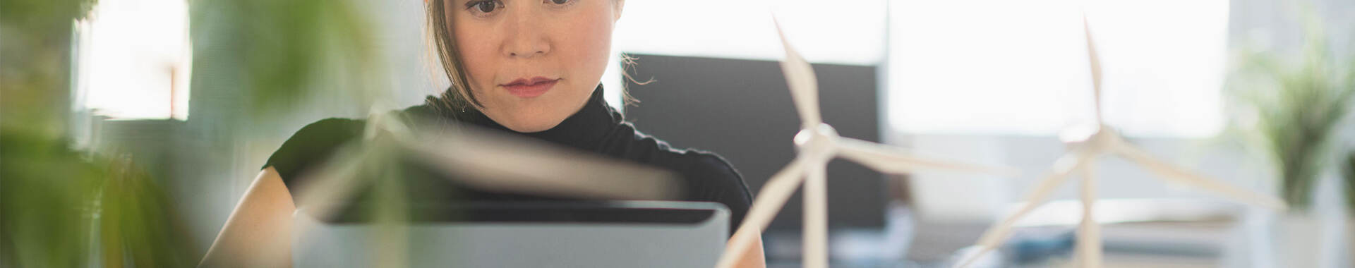 a person with small wind turbine models on a desk, working on a laptop