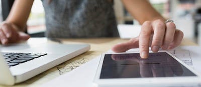 Close up of female architect at laptop using digital tablet in office