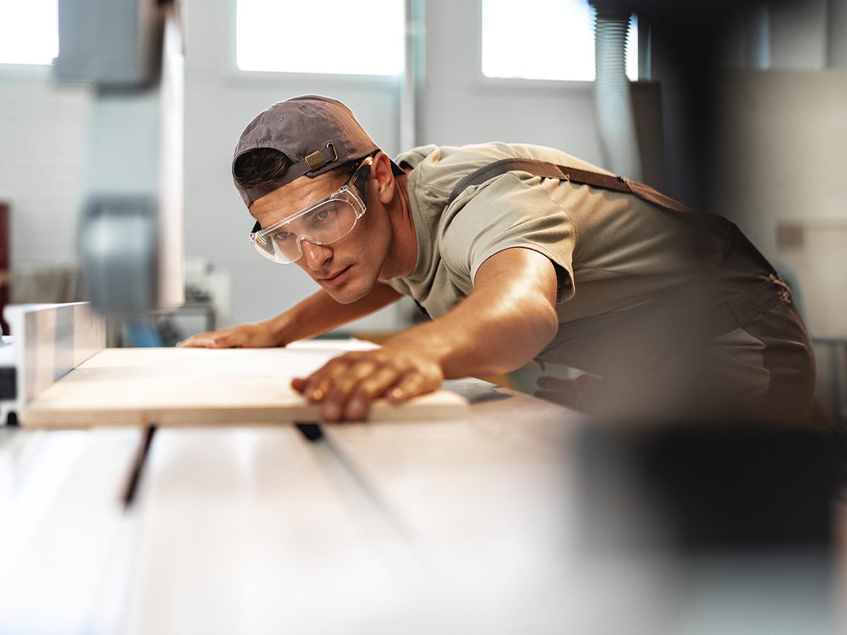 man with safety glasses lining a sheet of wood up for cutting on a table saw