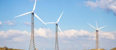 Wind turbines on a treeless hill under a blue sky with billowy clouds