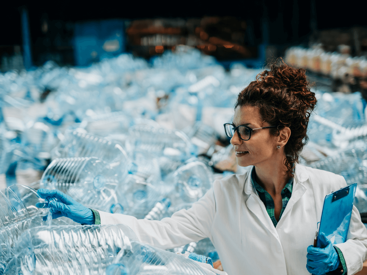 woman in lab coat inspecting pile of plastic bottles