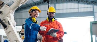 Engineers talking in a factory, with robotic arm in foreground